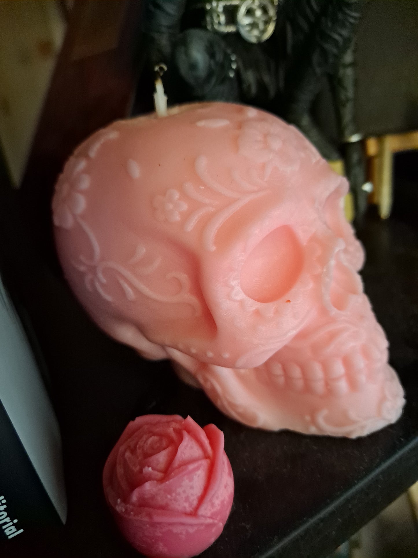 Vela rosa pálido en forma de calavera apagada en mi estantería con una pequeña flor de cera al lado
