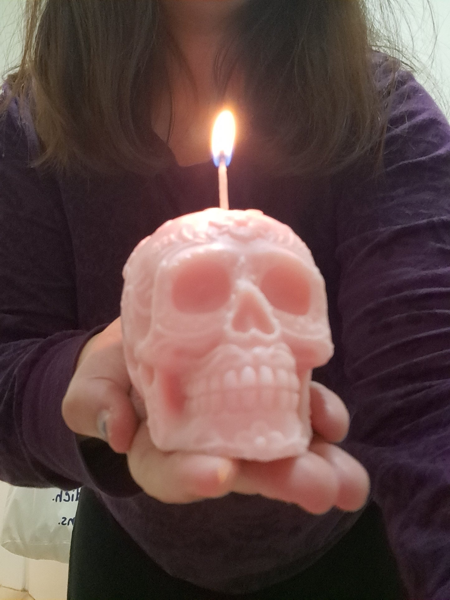 Vela rosa pálido con forma de calavera encendida en mi mano