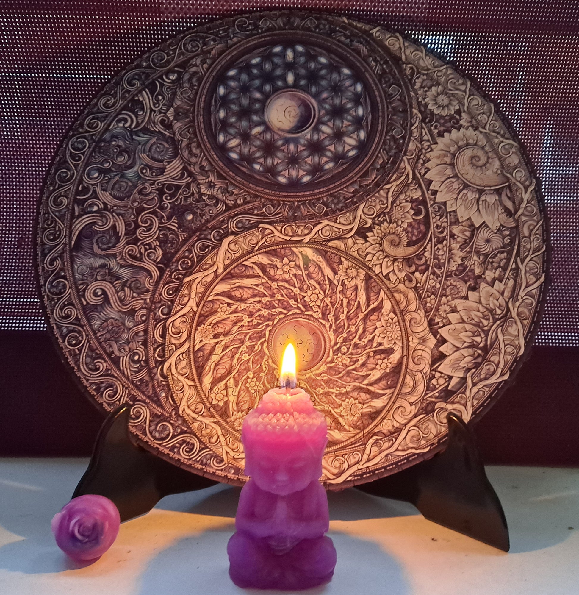 Vela de cera de abeja con forma de Buda, encendida, junto a una pequeña flor de cera y puzle Yin Yang detrás