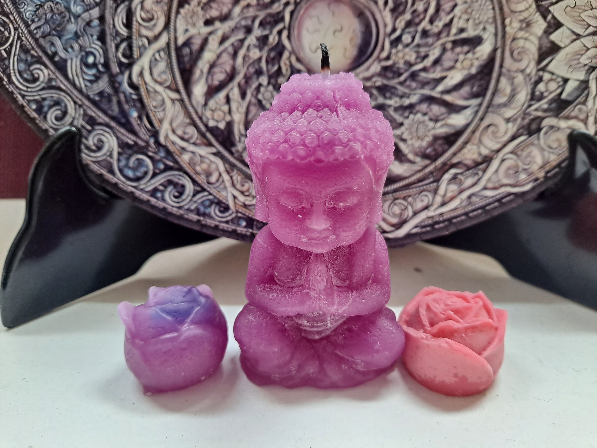 Vela de cera con forma de Buda, apagada, y dos pequeñas flores de cera 