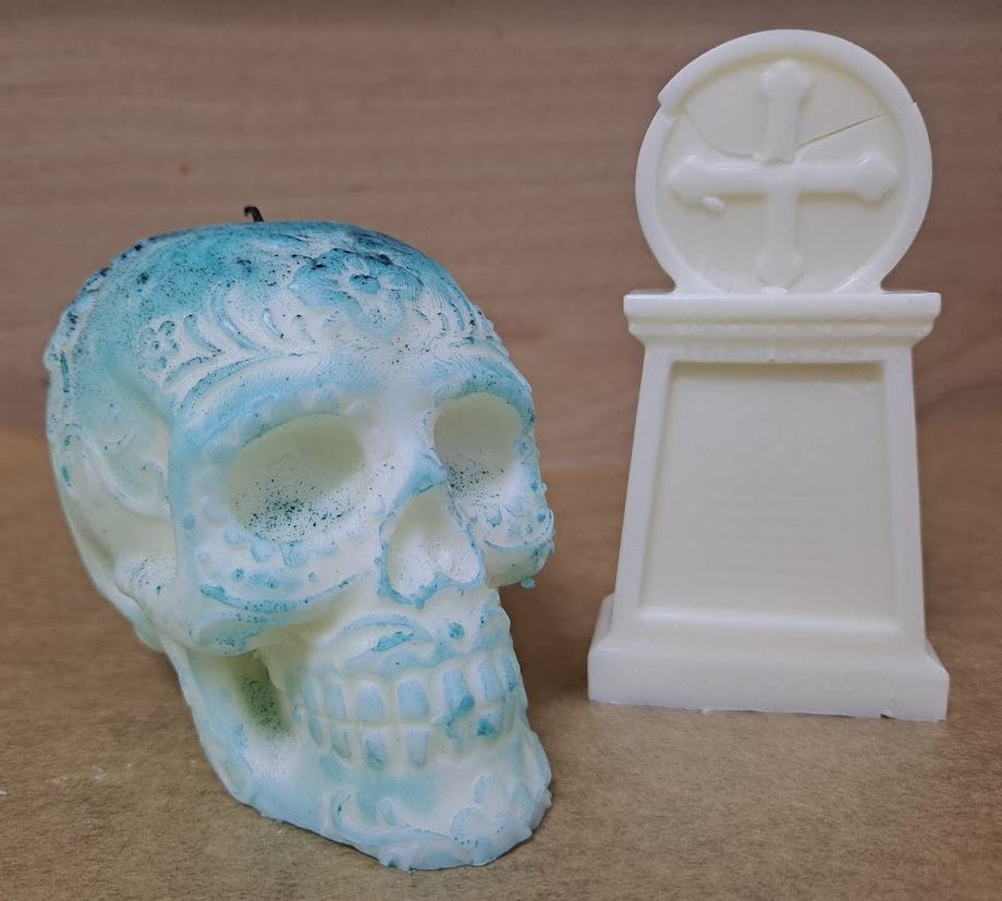 Vela blanca con detalles marcados en turquesa en forma de calavera con otra blanca en forma de lápida